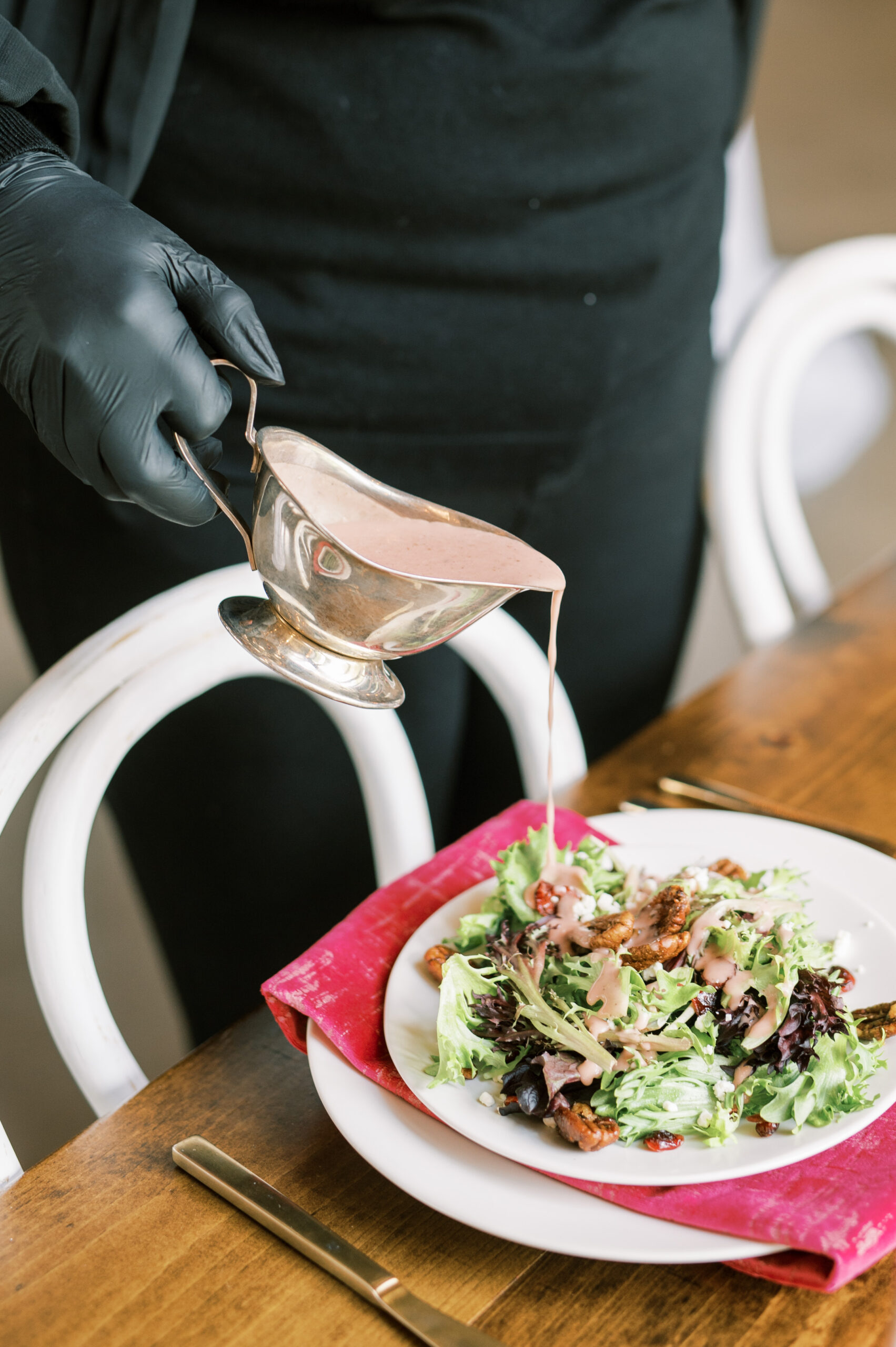 Caterer pouring vinaigrette over a plated salad