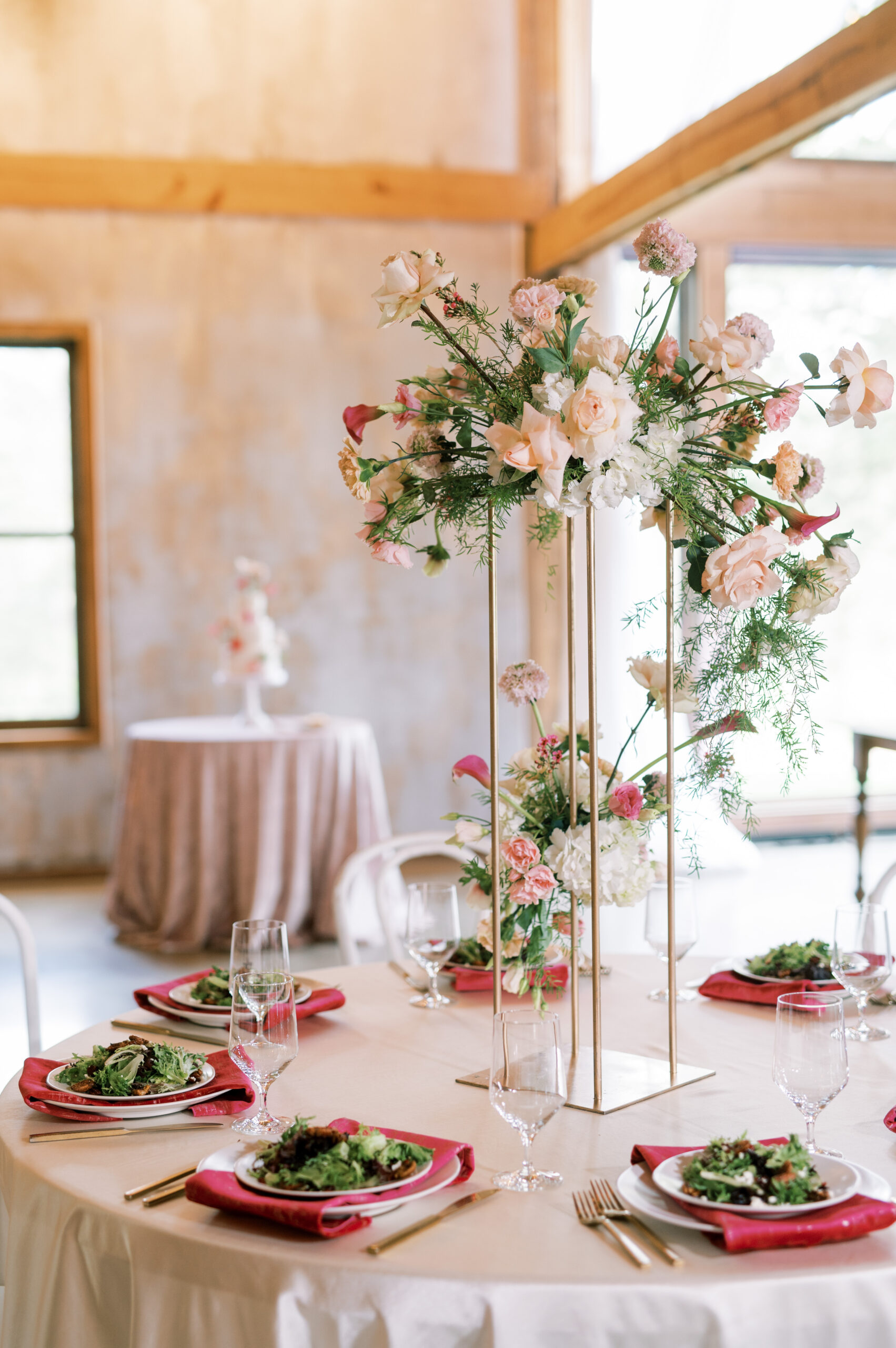 Plated salads at a reception table with an elevated centerpiece with a gold stand and a whimsical romantic flower arrangement