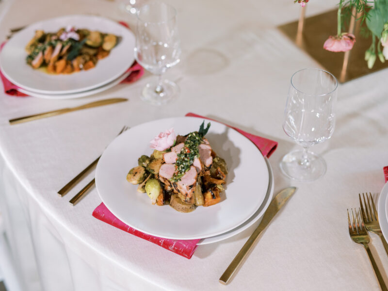 A wedding reception dinner on a white plate sitting on top of a pink napkin