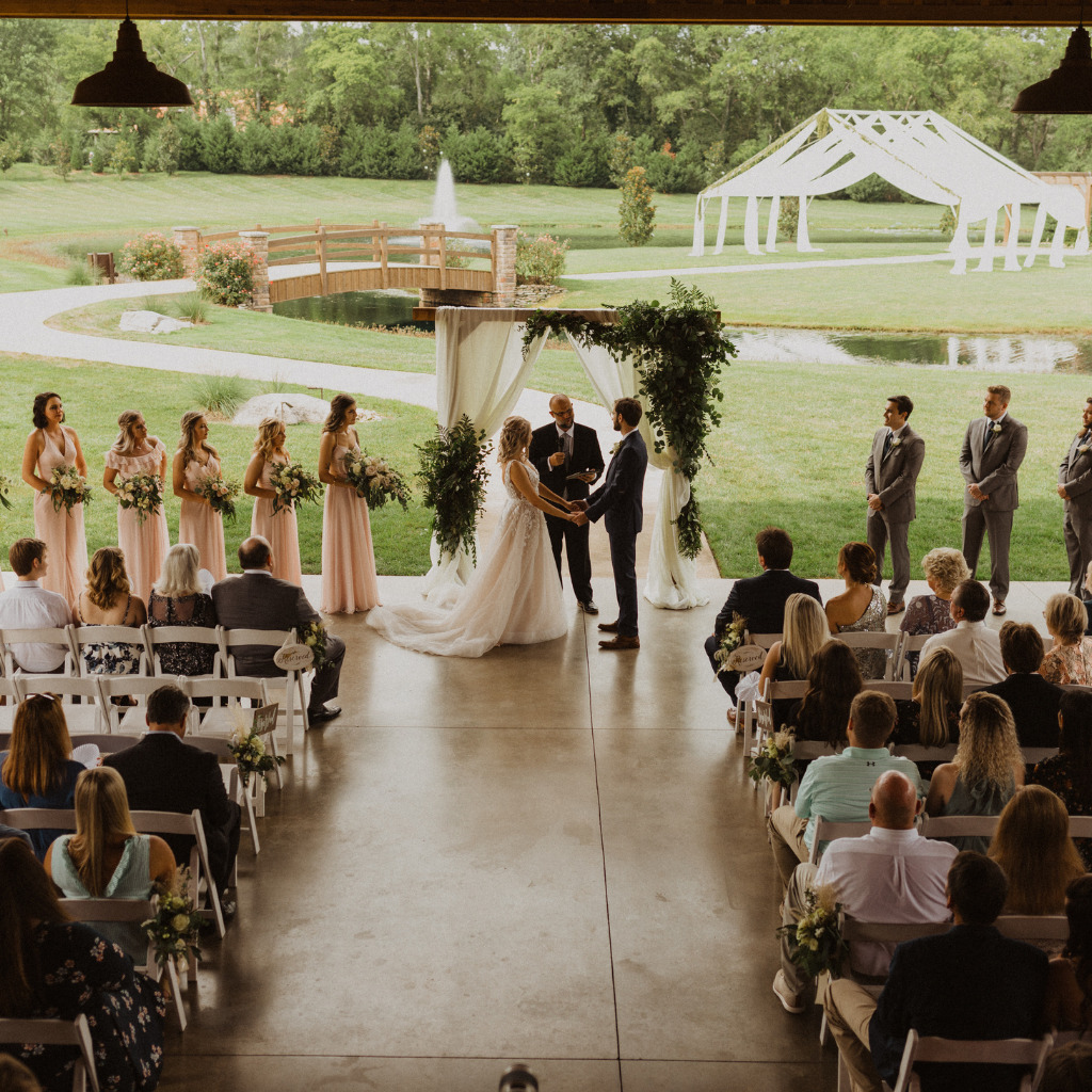 Outdoor Wedding Ceremony With Couple Holding Hands, Wedding Party And Guests