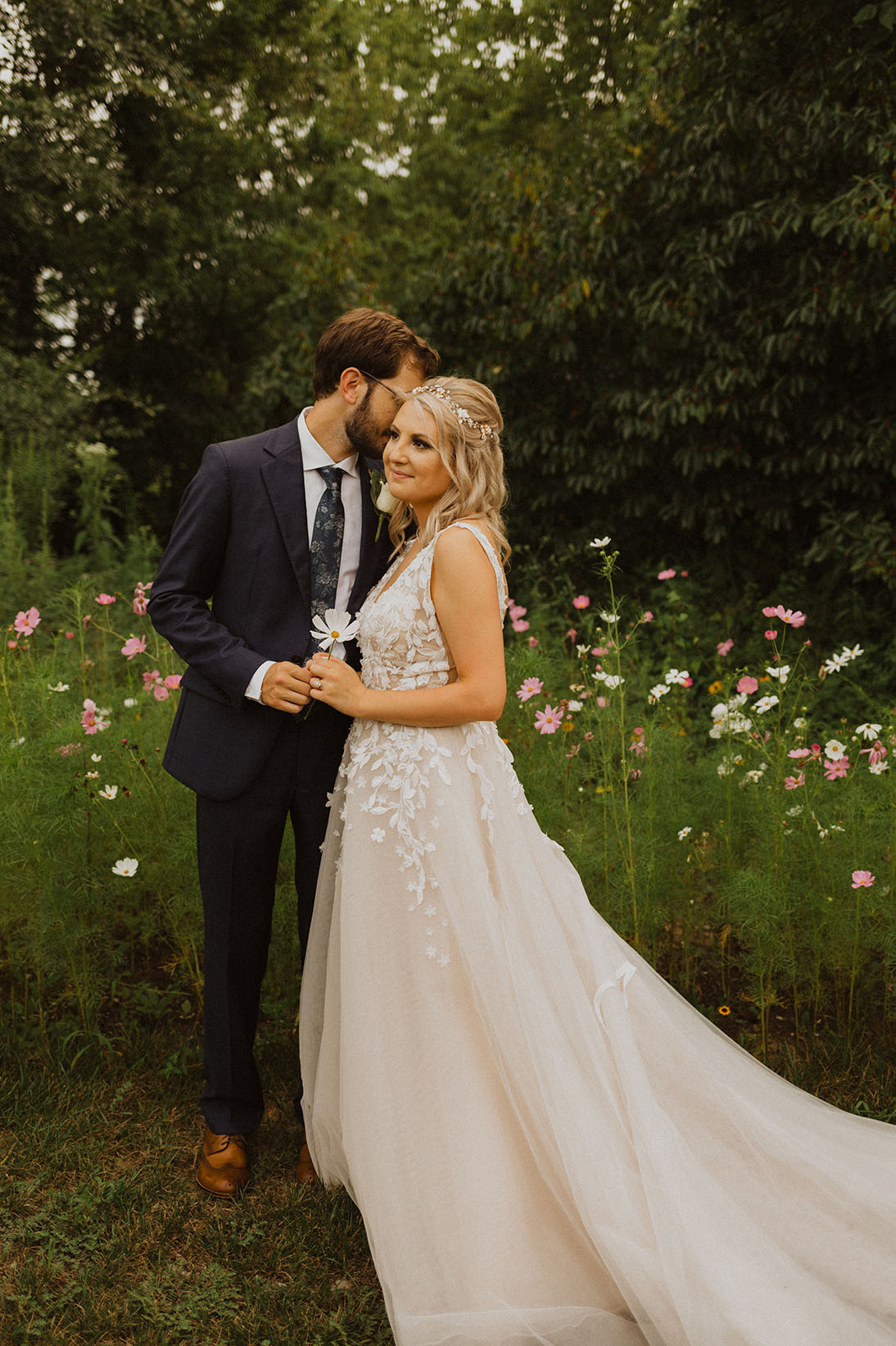 Bride Holding A Flower And Groom Kissing Bride In a Flower Field