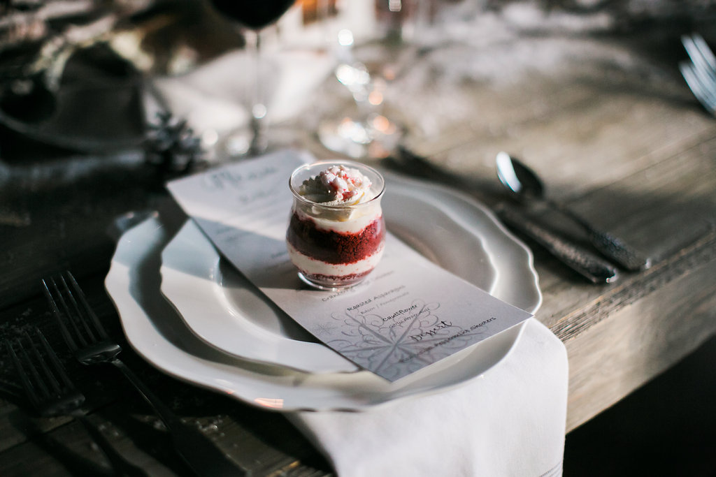 A red velvet dessert shooter sitting on a custom printed menu card at a holiday table place setting