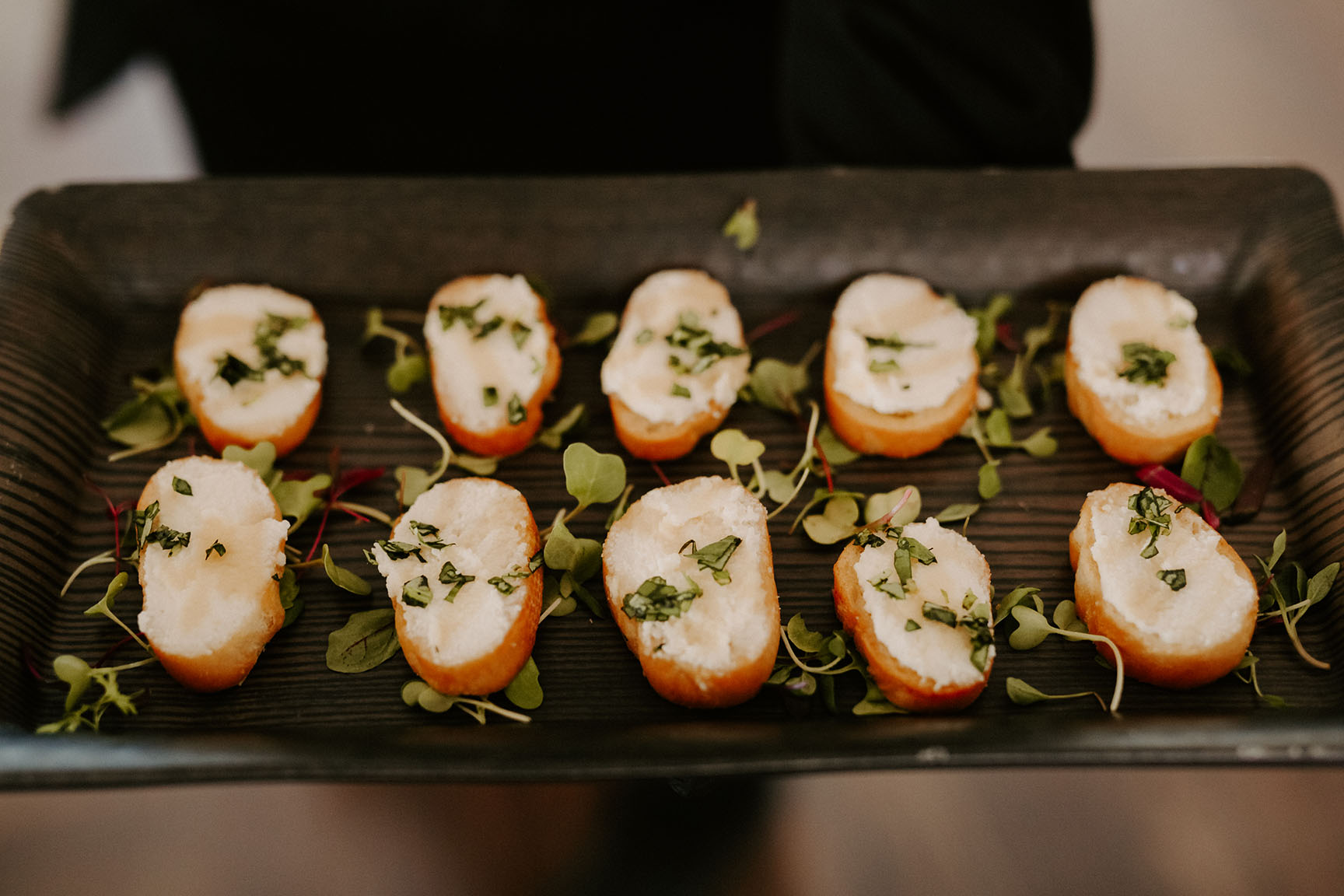 A close-up of a wedding cocktail hour appetizer of our tutti frutti crostini, made with ricotta, lemon, honey, and basil