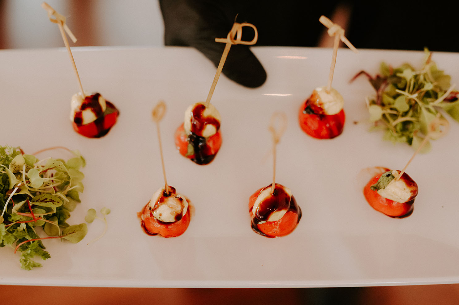 A close-up of a wedding cocktail hour appetizer of a caprese skewers, made with small tomatoes, bocconcini, and basil with a balsamic drizzle