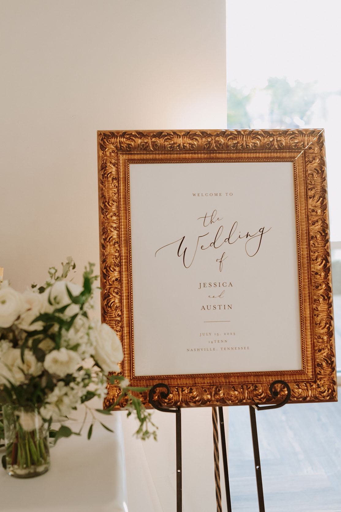 A wedding welcome sign with black text on a white board, framed in ornate gold