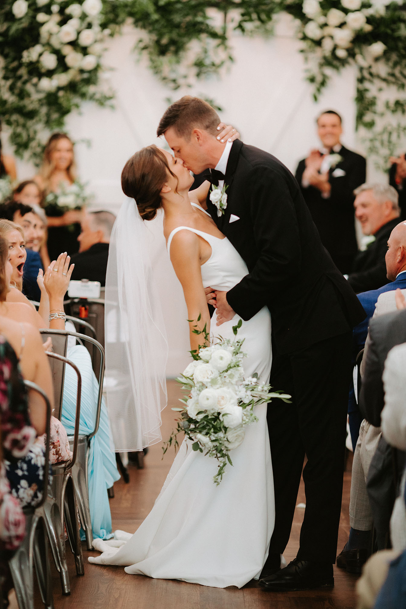 The bride and groom kiss mid-recessional while leaving their ceremony as guests clap and cheer