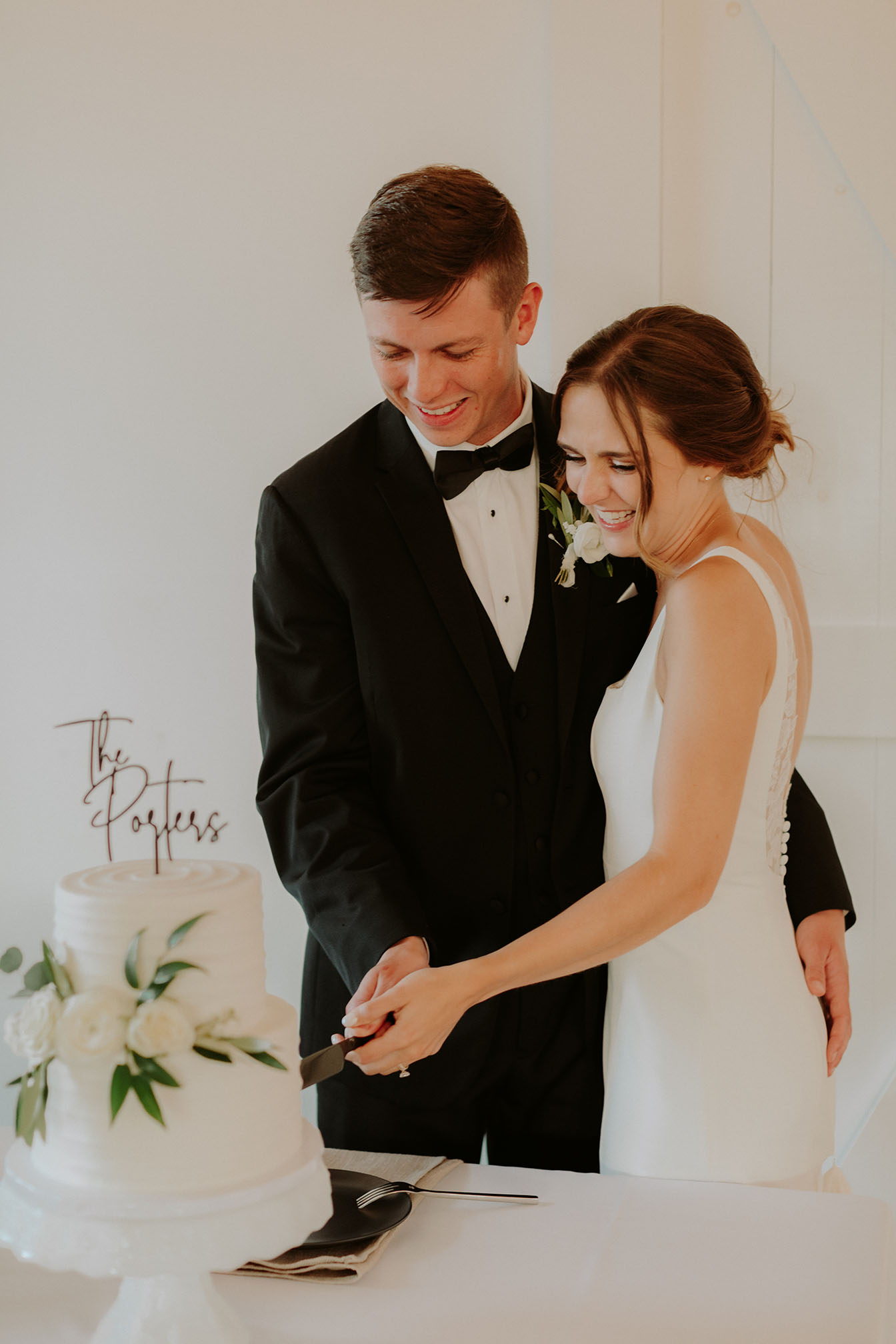 The bride and groom smile while cutting their two-tier classic white wedding cake together