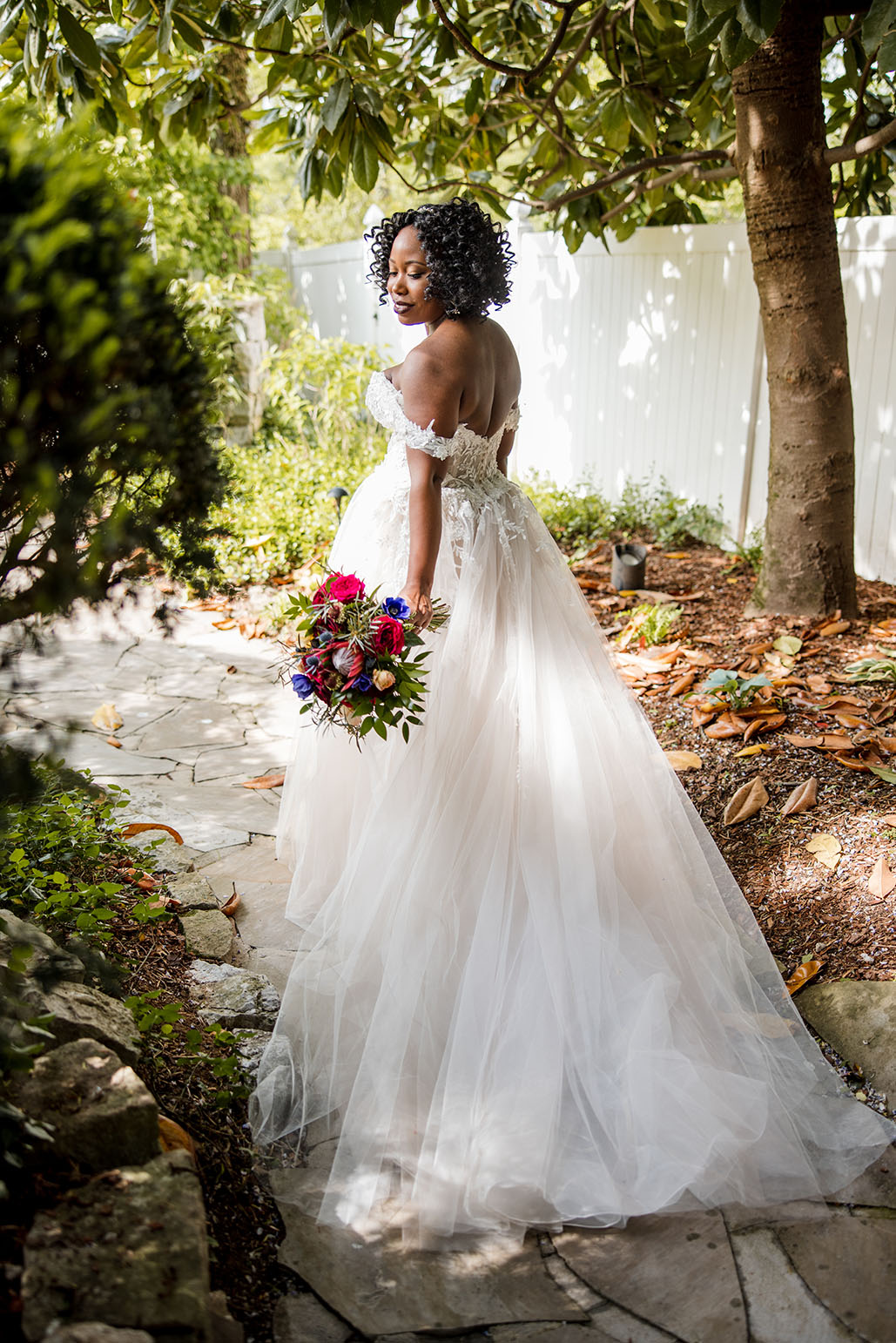 bride wearing open back lace wedding dress and holding a bright pink and blue bouquet