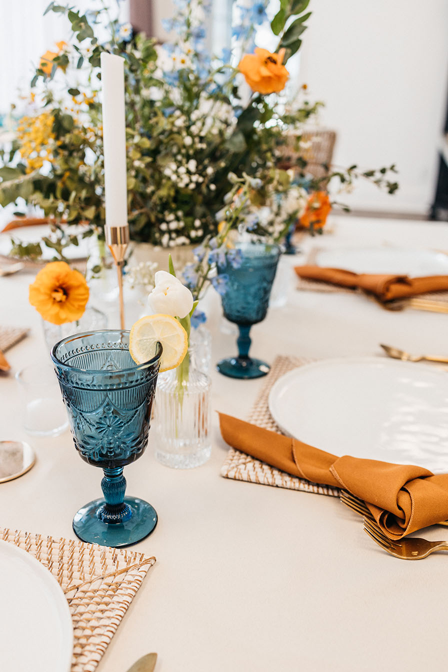 tablescape decor with blue goblet glassware and terracotta napkins and a colorful floral centerpiece