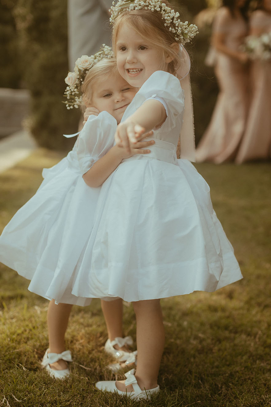 Two traditional flower girls in white smock dresses, mary jane shoes, and white flower crowns