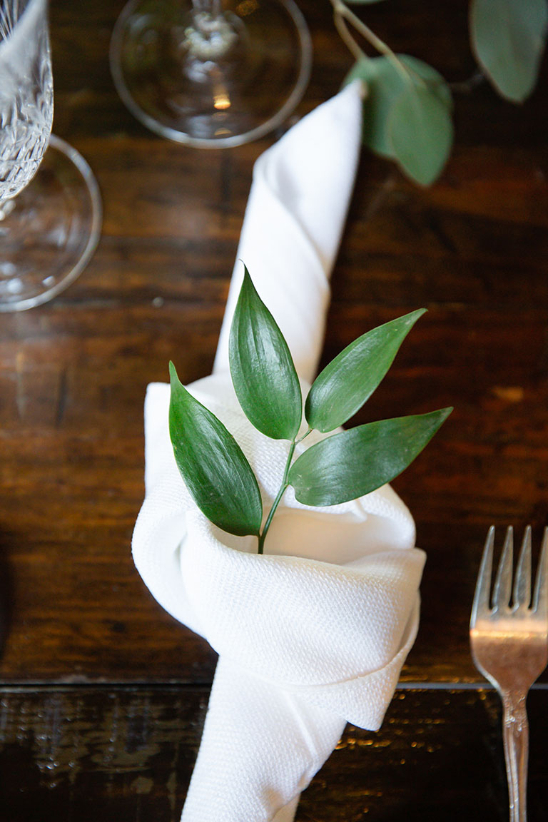 Close-up image of greenery sprig in knotted white napkin