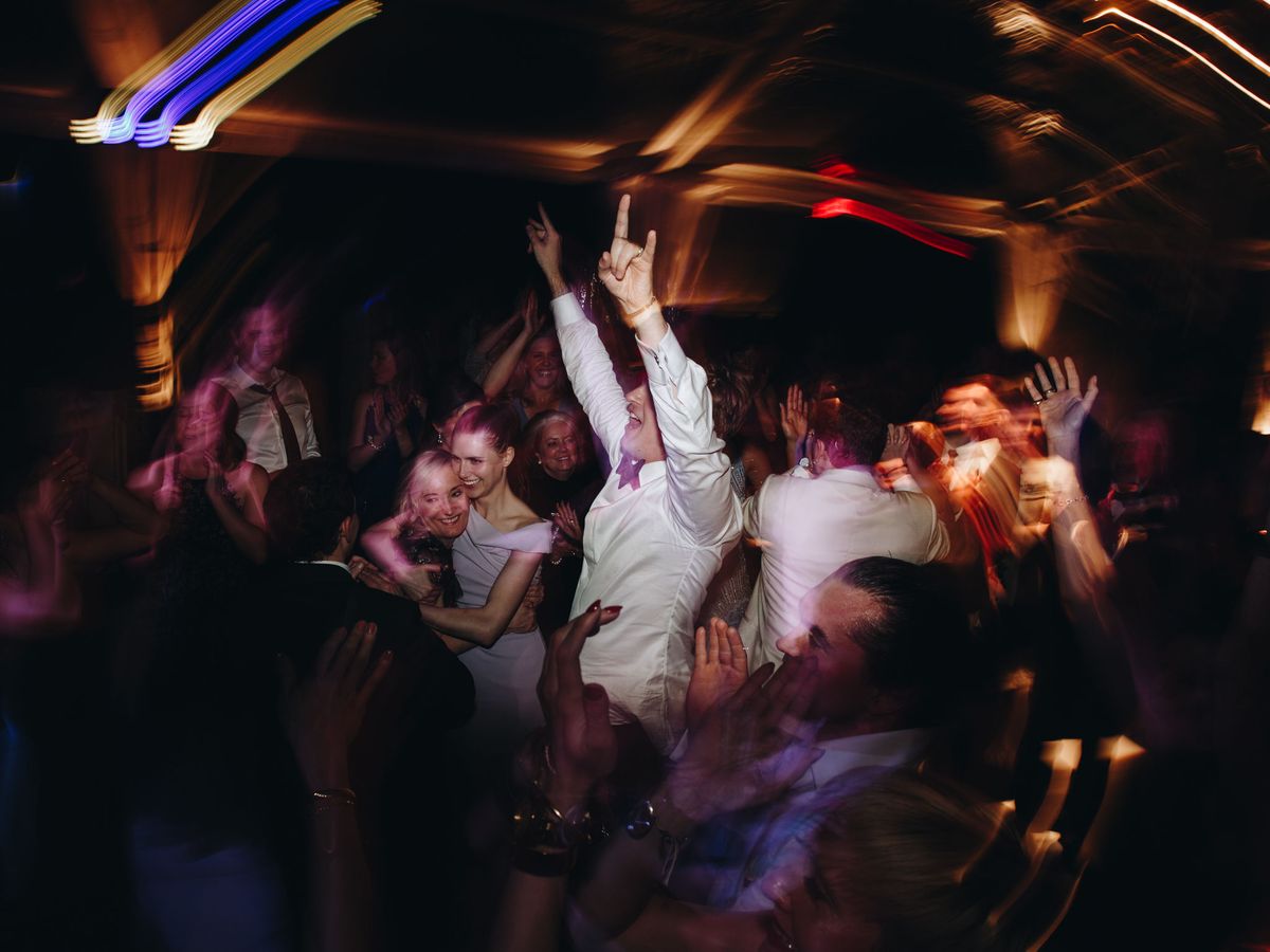 Nighttime wedding photography of a wedding guest cheering with their arms up in the middle of the dance floor