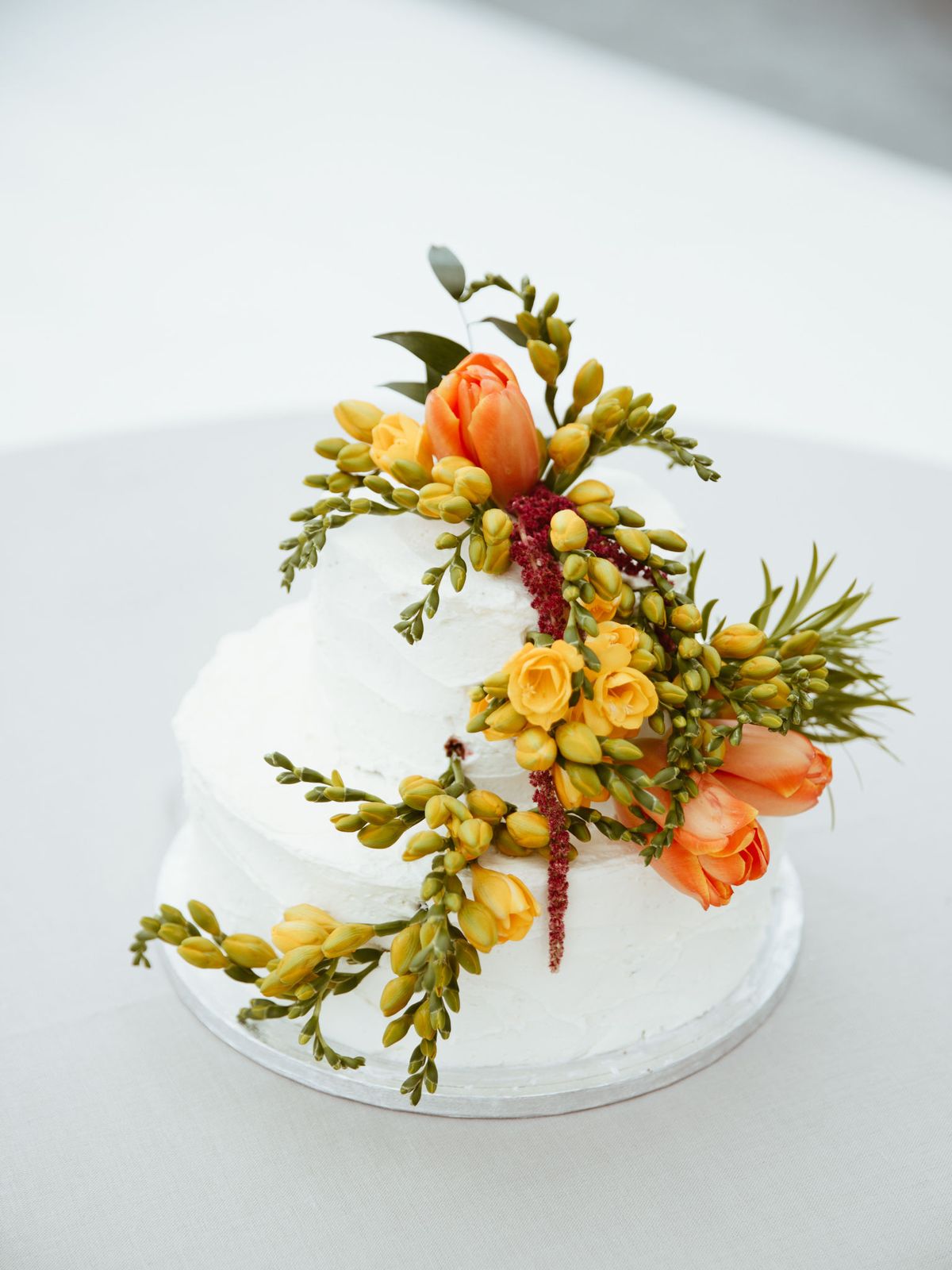 A two-tier white wedding cake with bright yellow and orange flowers draped along the side