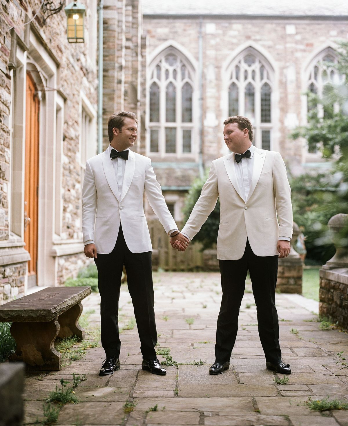 Two grooms hold hands and look at each other outside of their ceremony venue, the Scarritt Bennett Center