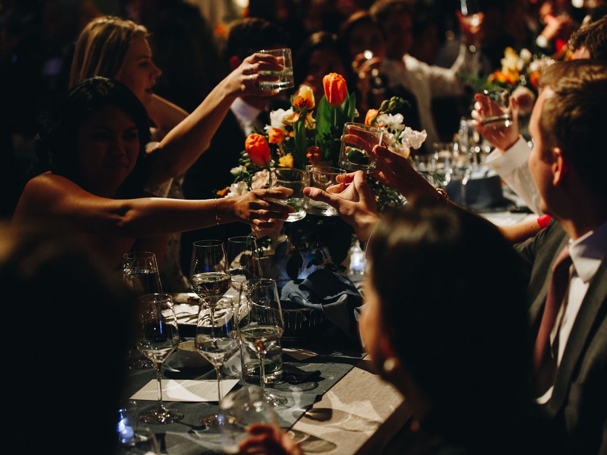 Nighttime wedding photography of guests toasting their glasses across a reception table with colorful floral centerpieces