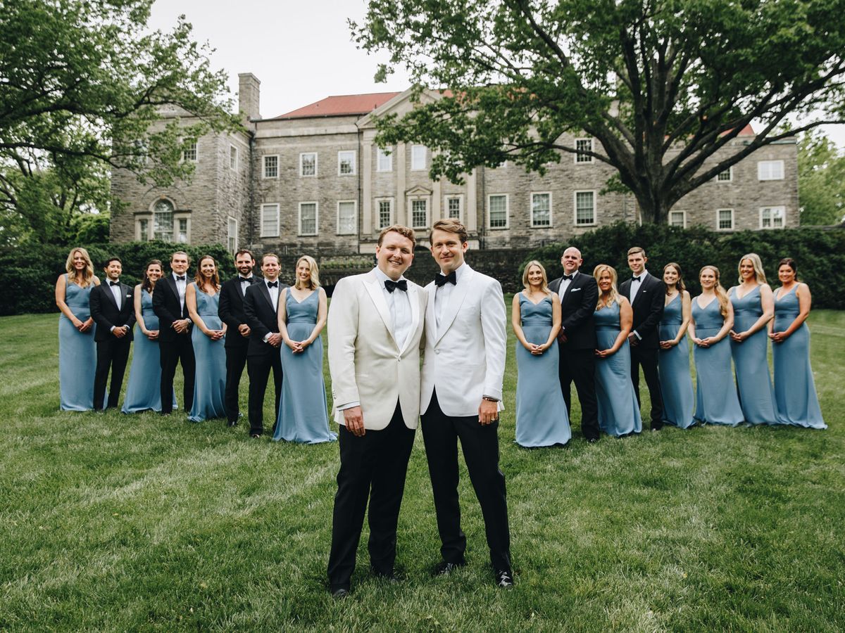 Two grooms stand in the forefront with their wedding party behind them