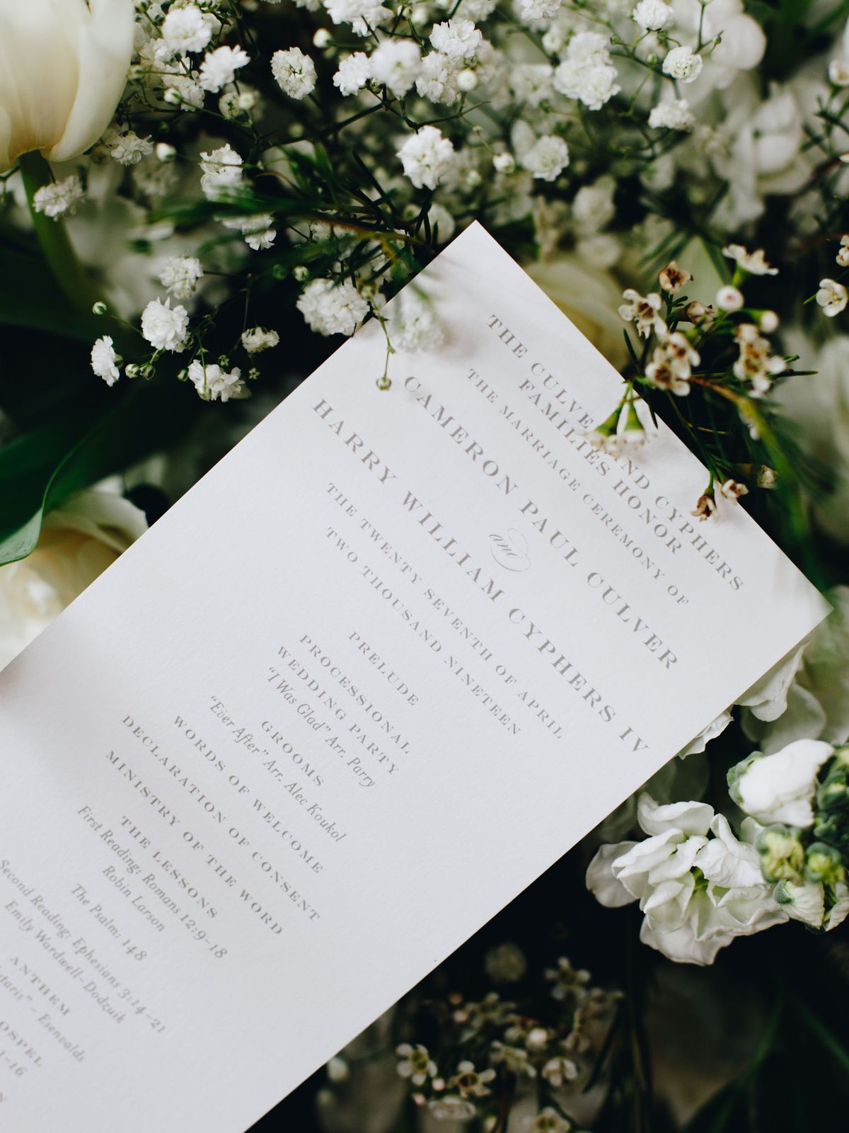 A close-up of a wedding ceremony program sitting on top of baby's breath floral arrangement