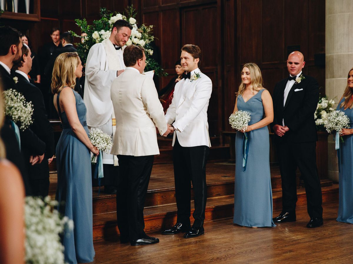 Two grooms hold hands at the altar during their wedding ceremony