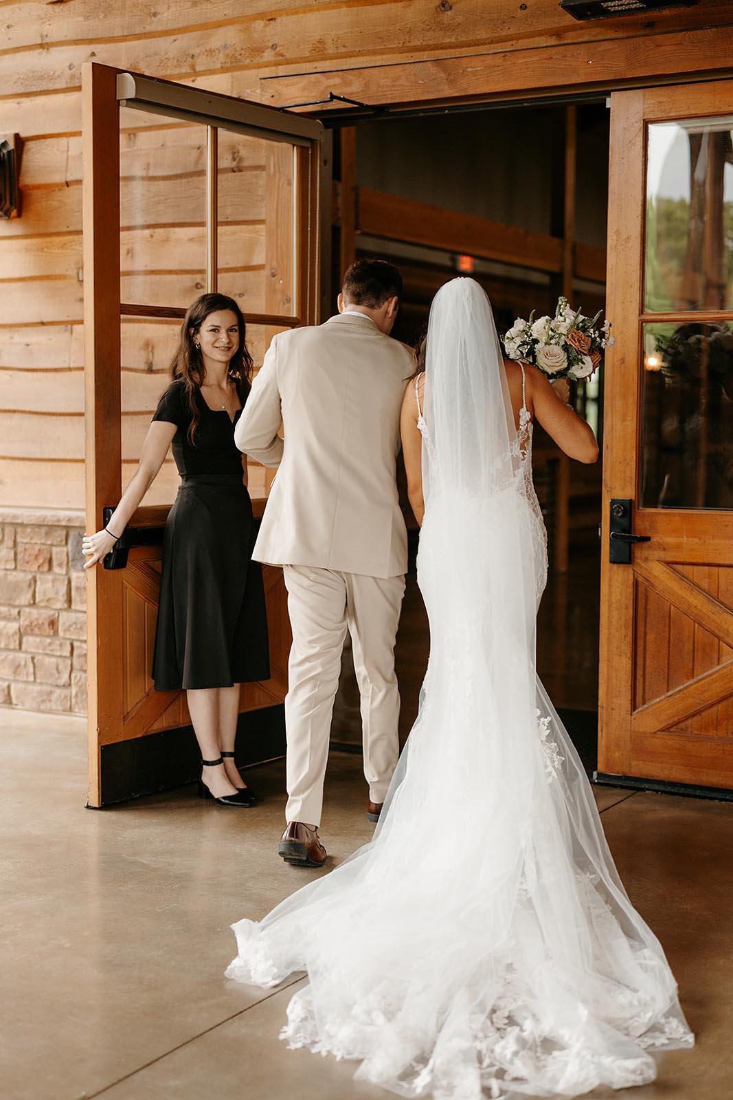 The event planner holds the door for the bride and groom as they enter their barn reception