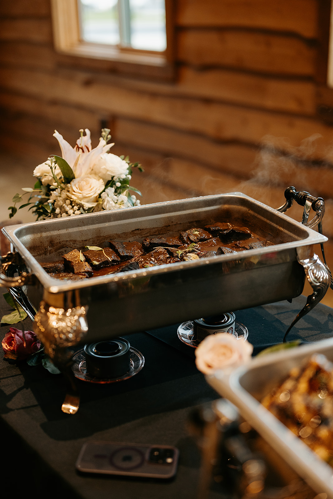 Garlic rosemary braised beef in a chafing dish set up on a buffet table with a white floral arrangement