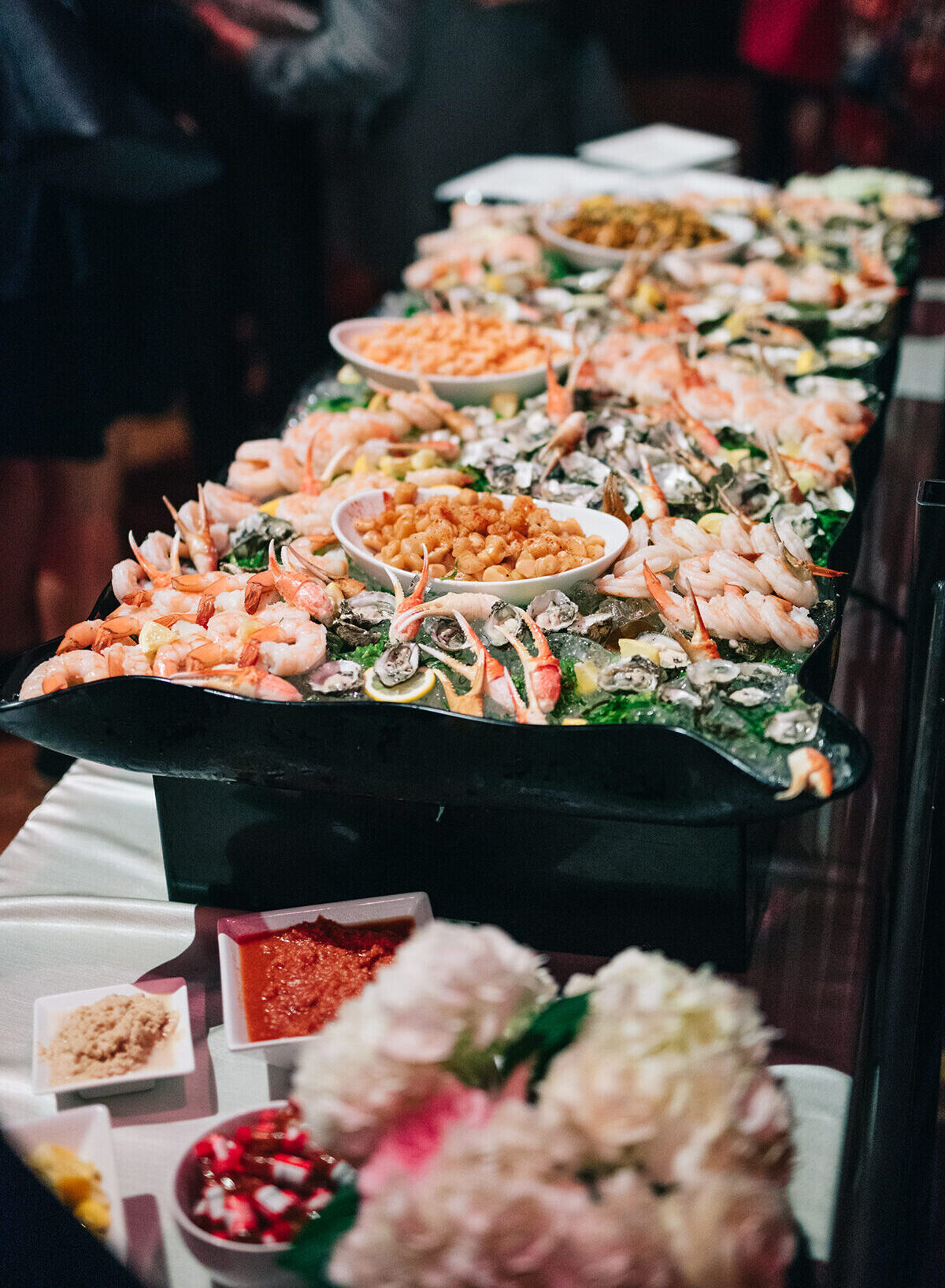 Seafood display of chilled shrimp, oysters and crab claws on ice, with cocktail sauce and horseradish at an event reception