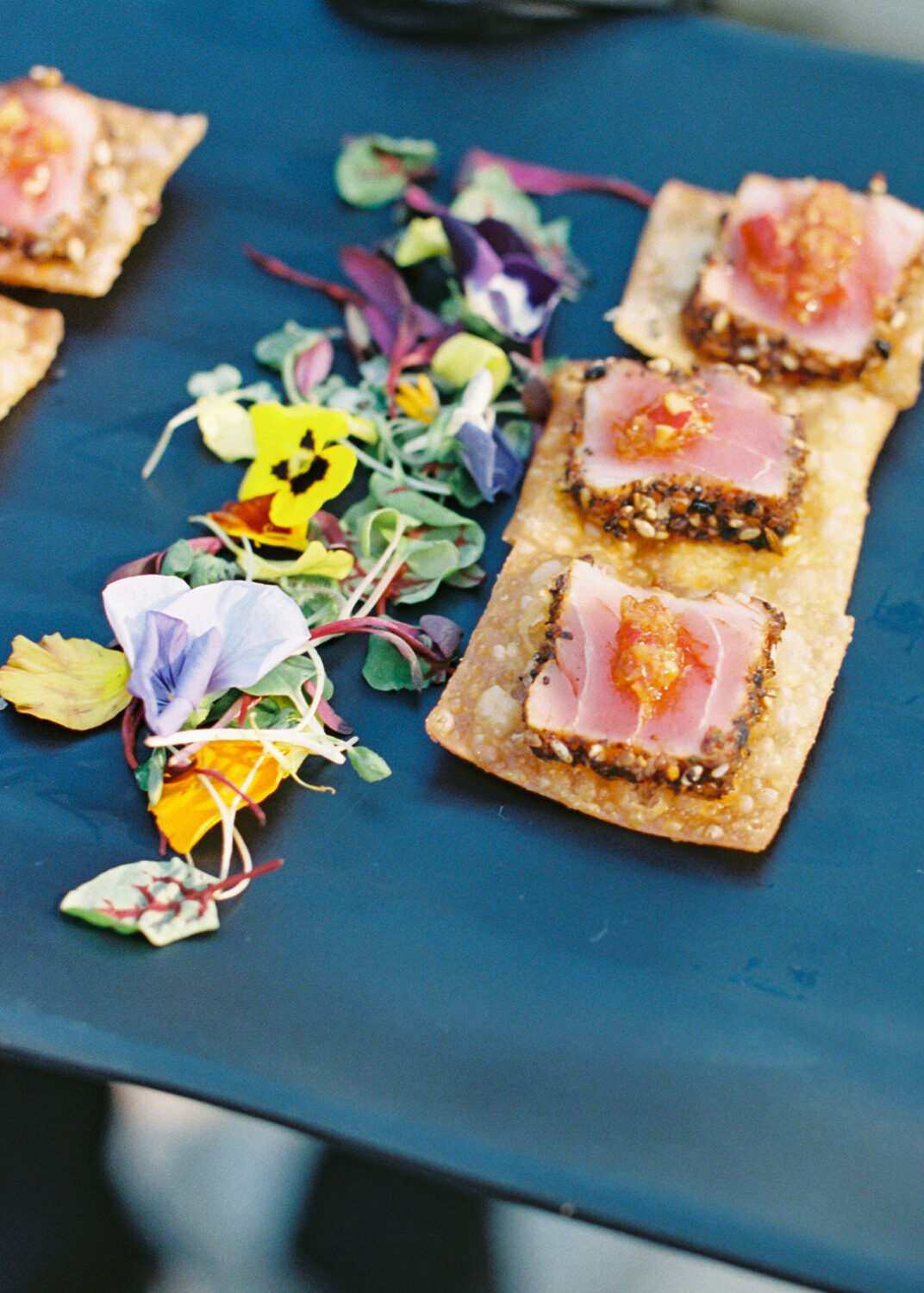 Sesame-crusted seared tuna on crispy wonton chips topped with chili relish, served with microgreens and edible flowers