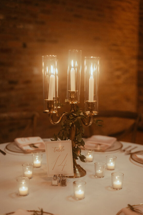 Antique brass candelabra centerpiece with white taper candles surrounded by small white votive candles at center of wedding reception table